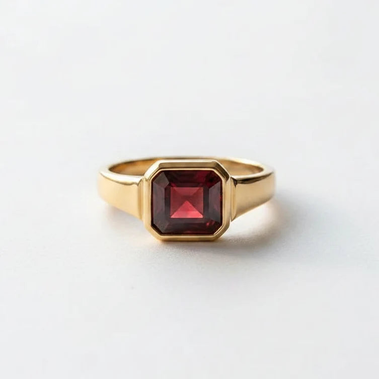 A gold signet ring with a faceted dark red gemstone resting on an open vintage book with printed text and astrological diagrams.