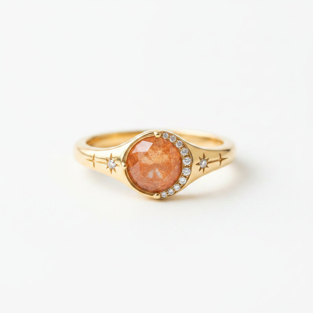 A gold signet ring with a round, faceted orange-brown gemstone and small clear accent stones, resting on a rustic wooden surface.