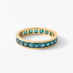 Gold ring with green gemstones on a textured surface with lavender