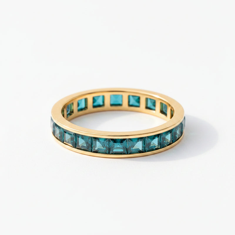 Gold ring with green gemstones on a textured surface with lavender