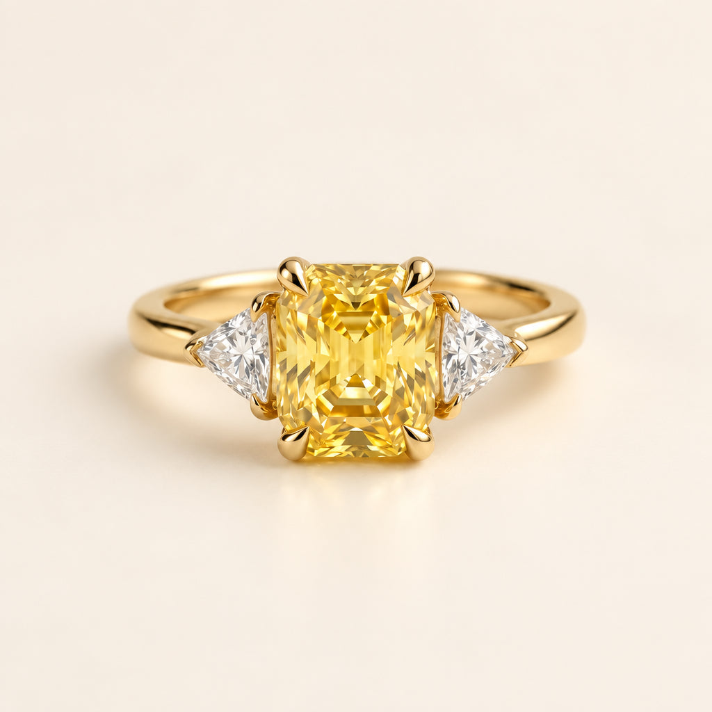 Gold ring with a yellow gemstone and two smaller diamonds on a textured surface with green leaves in the background.