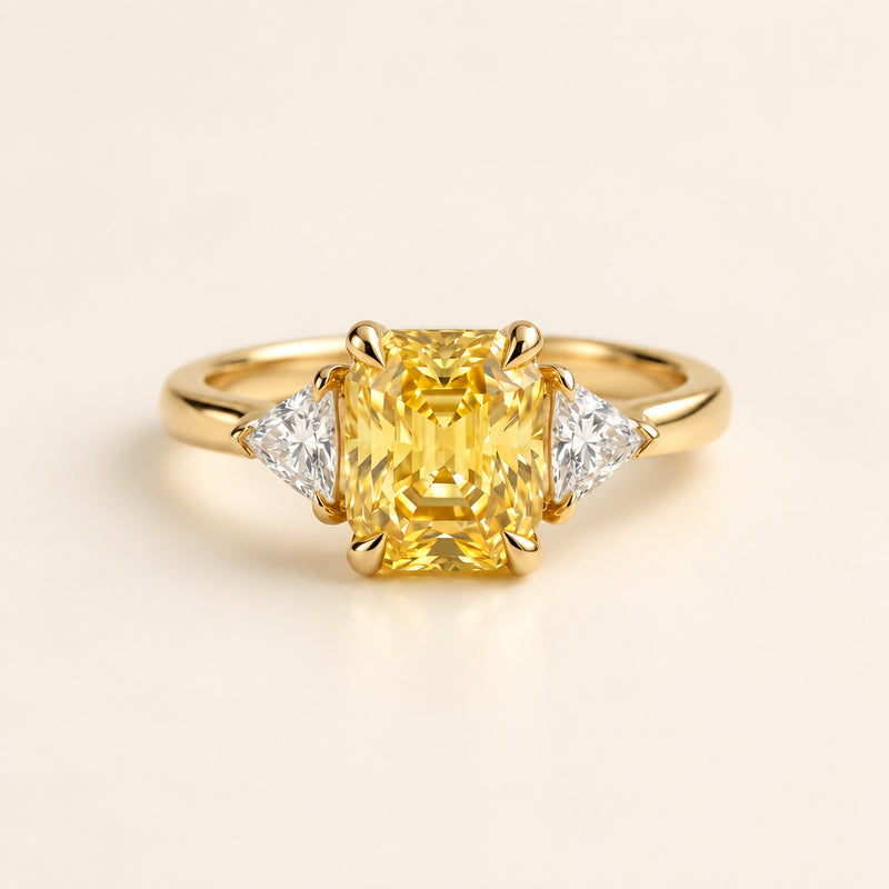 Gold ring with a yellow gemstone and two smaller diamonds on a textured surface with green leaves in the background.