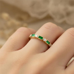 Gold ring with green gemstones on a finger against a neutral background
