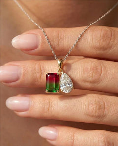 Gold necklace with a green and red gemstone pendant held by a hand.