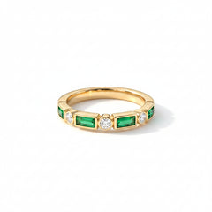 Gold ring with emeralds and diamonds on a textured surface with dried flowers.