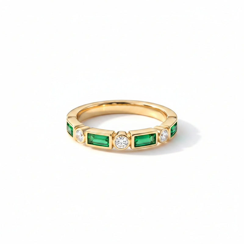 Gold ring with emeralds and diamonds on a textured surface with dried flowers.