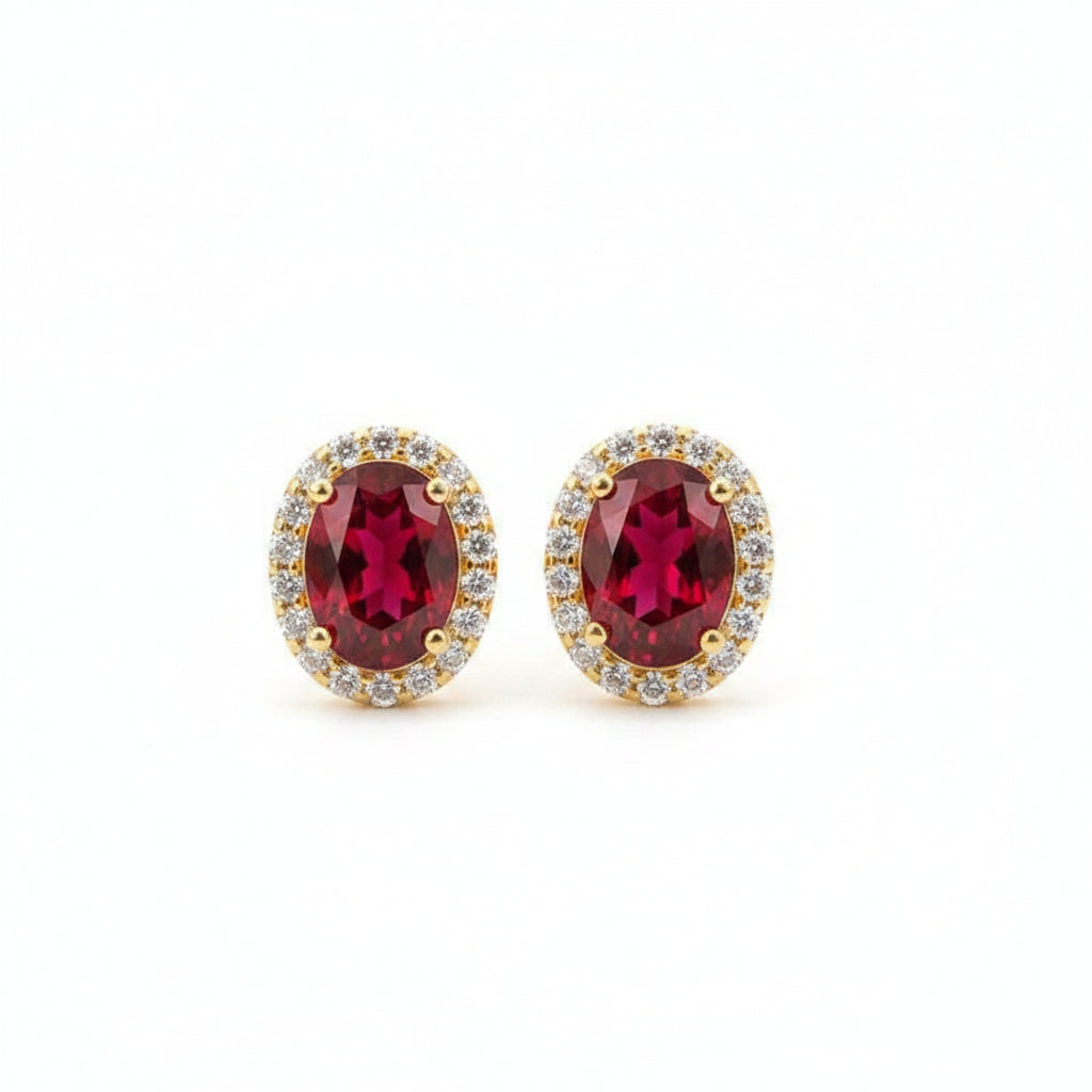 Gold earrings with red gemstones on a textured surface with dried flowers.