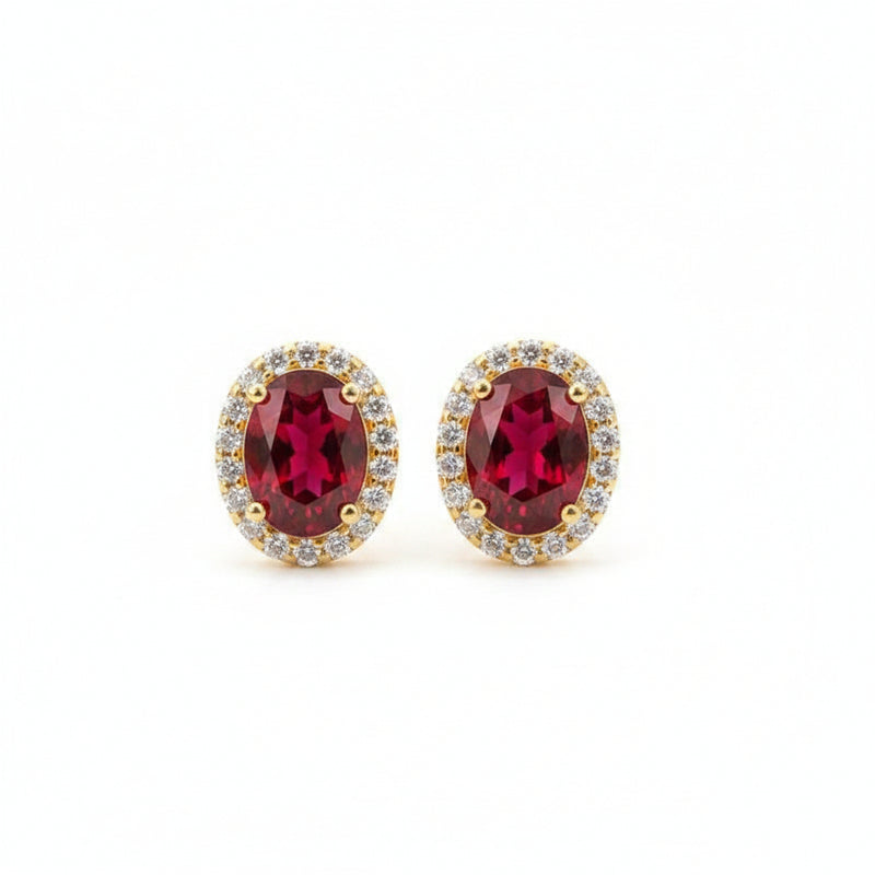 Gold earrings with red gemstones on a textured surface with dried flowers.