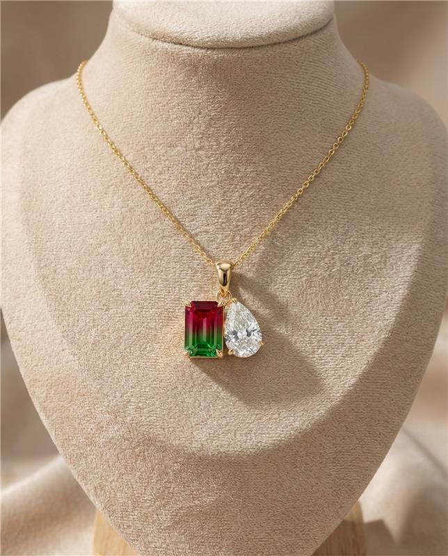 Gold necklace with a green and red gemstone pendant on a beige mannequin.