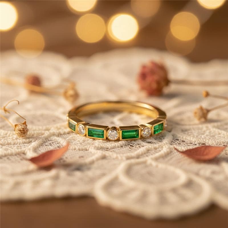 Gold ring with emeralds and diamonds on a textured surface with blurred lights in the background