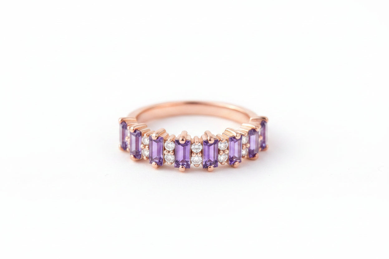 Rose gold ring with purple gemstones on a textured fabric background with flowers.