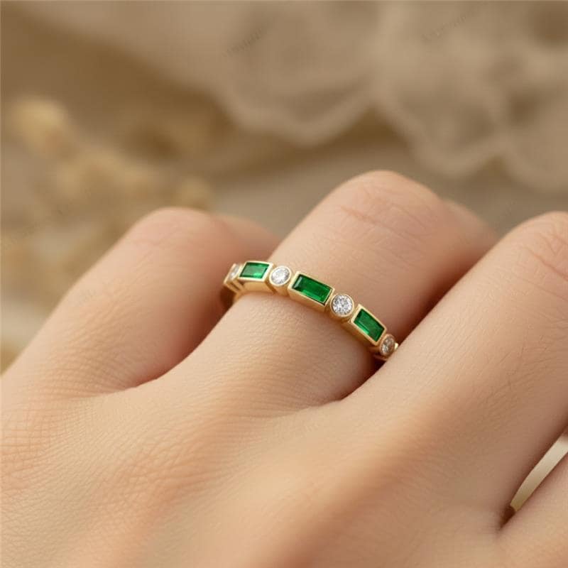 Gold ring with green gemstones on a finger against a neutral background