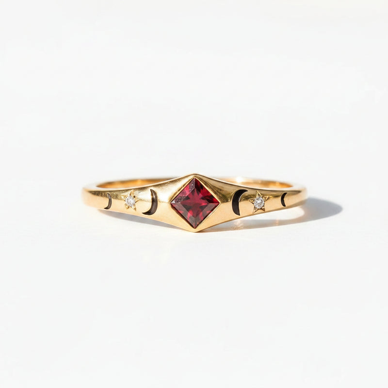 A gold ring with a central red gemstone and small side details, resting on a rustic wooden surface under warm light.