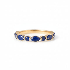 A gold ring featuring a row of oval-cut deep blue lapis lazuli stones, displayed on a light gray and white marble surface.