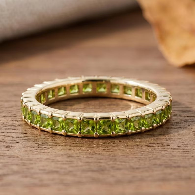 A gold eternity ring featuring a row of green peridot gemstones, resting on a rustic wooden surface.