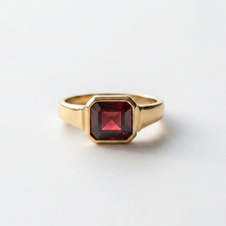 A gold signet ring with a faceted dark red gemstone resting on an open vintage book with printed text and astrological diagrams.