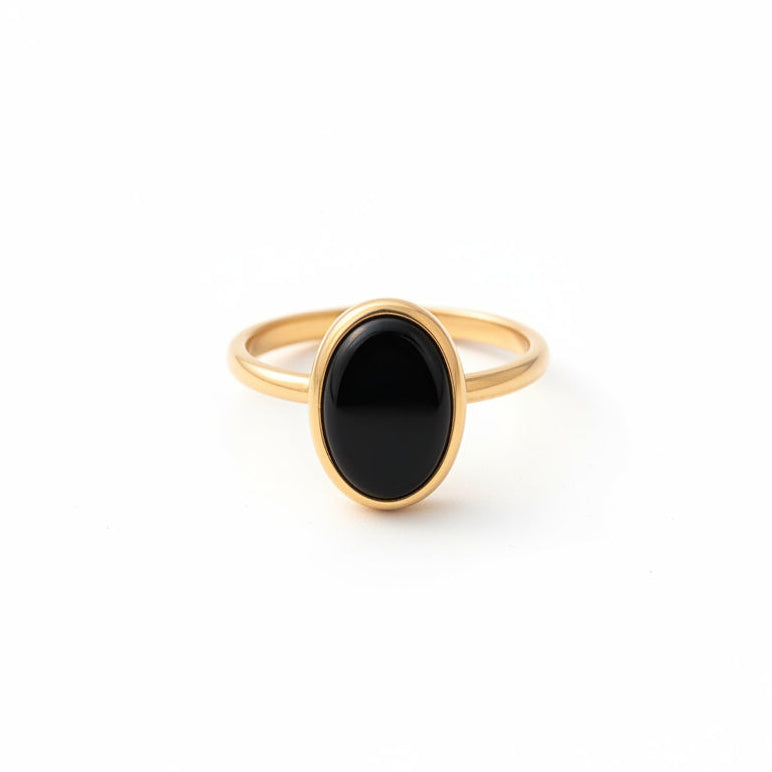 Gold ring with a black stone on a textured fabric background with dried flowers.