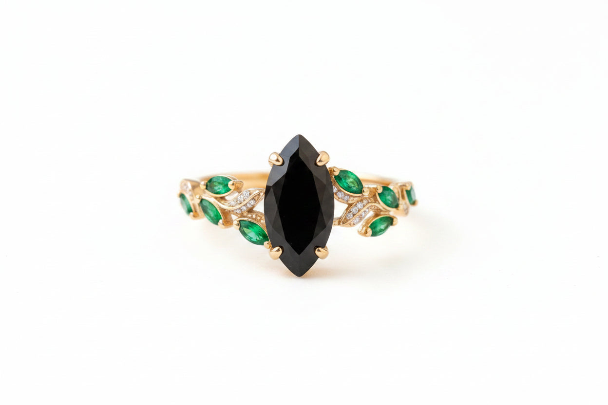Gold bracelet with a black gemstone and green stones on a textured surface with flowers.