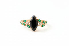 Gold bracelet with a black gemstone and green stones on a textured surface with flowers.