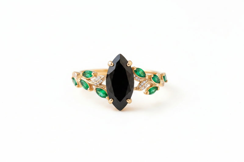 Gold bracelet with a black gemstone and green stones on a textured surface with flowers.