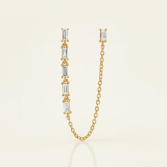 A gold chain necklace featuring a vertical bar with five baguette-cut clear stones in gold settings, shown on a white background with a faint diagonal grid pattern.