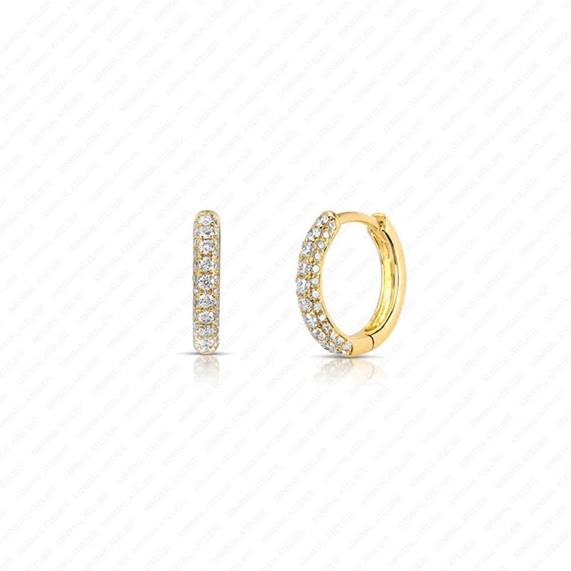 A pair of gold huggie hoop earrings adorned with pavé-set clear stones, shown from two angles on a white background with a faint diagonal grid pattern.