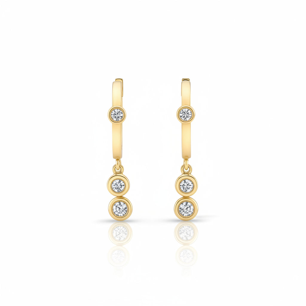 A pair of gold huggie hoop earrings with three small round-cut gemstones on each earring, displayed against a light gray patterned background.