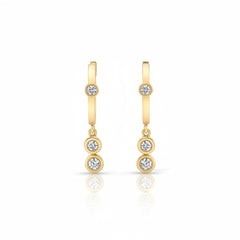 A pair of gold huggie hoop earrings with three small round-cut gemstones on each earring, displayed against a light gray patterned background.