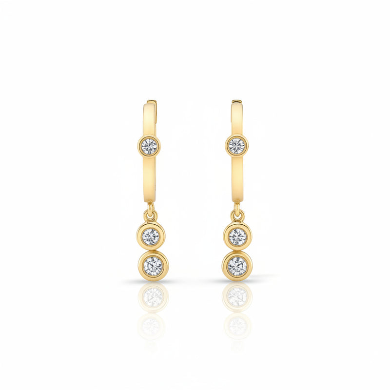A pair of gold huggie hoop earrings with three small round-cut gemstones on each earring, displayed against a light gray patterned background.