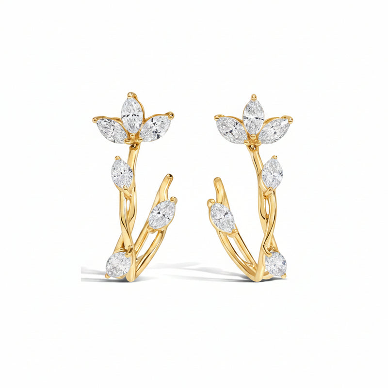 A pair of gold huggie hoop earrings decorated with marquise-cut clear gemstones arranged in a leafy branch design, shown on a white background with a faint diagonal watermark pattern.