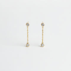 A pair of gold chain drop earrings with small clear gemstone accents, displayed on a light textured background.