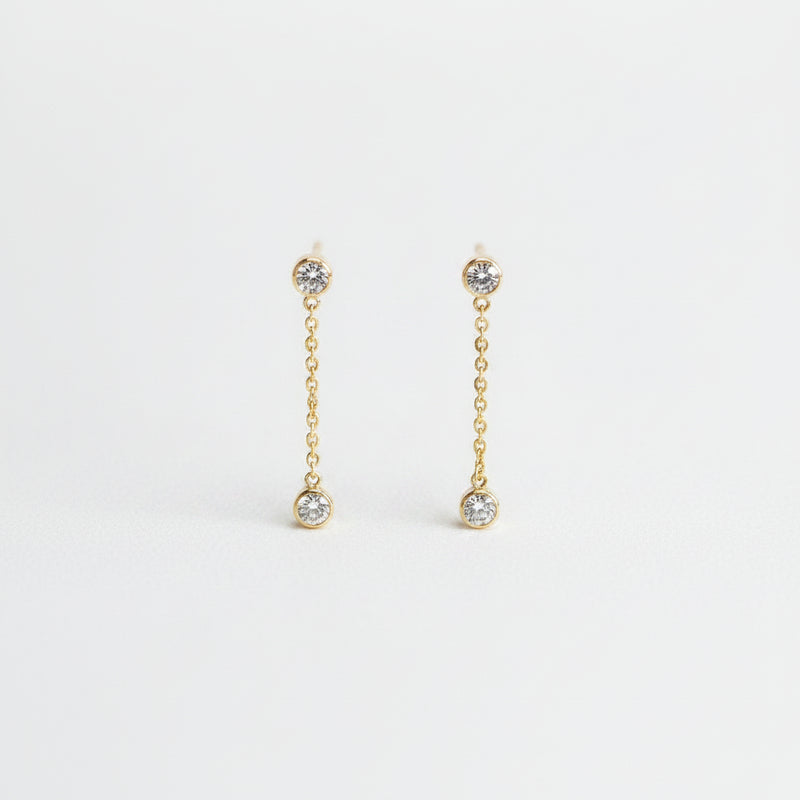 A pair of gold chain drop earrings with small clear gemstone accents, displayed on a light textured background.