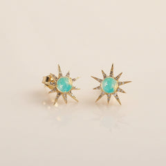 A pair of gold starburst stud earrings with oval light blue-green opal centers, displayed on a light gray background with a faint repeating watermark.