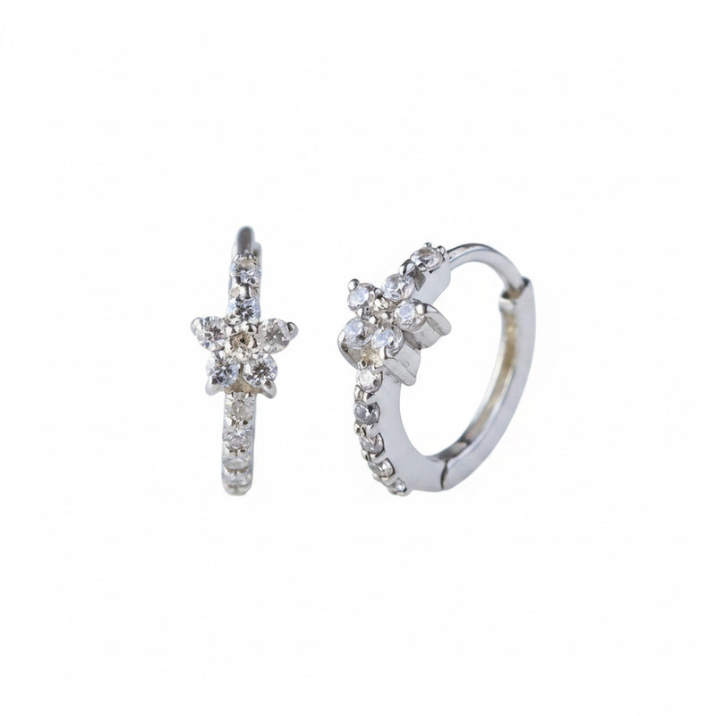 A pair of silver huggie hoop earrings decorated with small clear crystals, displayed on a light gray reflective surface.