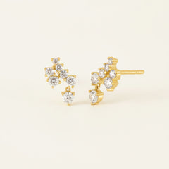 A pair of gold stud earrings with clear gemstones, shown on a white background with a faint diagonal watermark pattern.