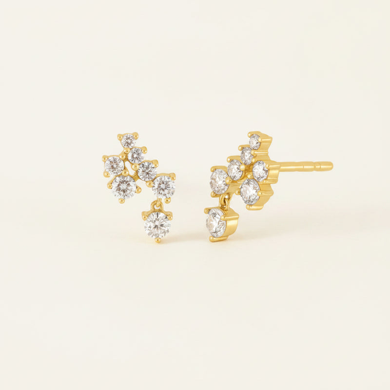 A pair of gold stud earrings with clear gemstones, shown on a white background with a faint diagonal watermark pattern.