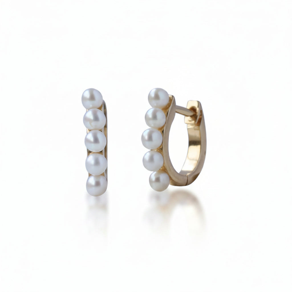 A pair of gold huggie hoop earrings decorated with five white freshwater pearls on each earring, shown against a white background with a faint diagonal watermark pattern.