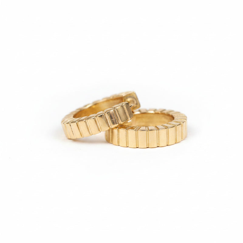 Two gold rings with a textured, ribbed outer edge and smooth inner band, displayed on a white textured surface with a repeating 'MINIMAL ATELIER' watermark.