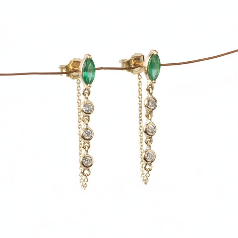 A pair of gold dangle earrings with marquise-cut green gemstones and clear round stones on a chain, displayed against a white background with a diagonal watermark pattern.
