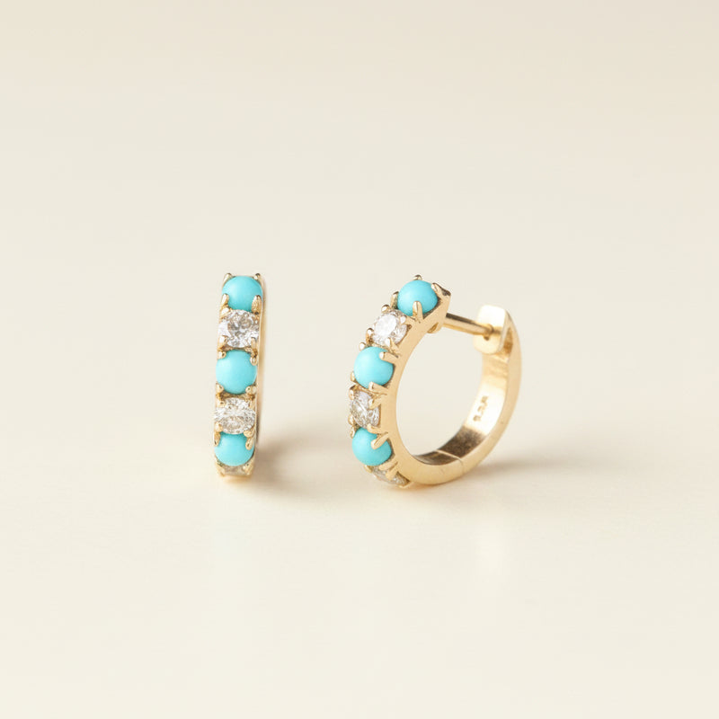 A pair of gold huggie hoop earrings with five round turquoise-blue stones and small clear crystals, displayed on a light gray background with a repeating 'MINIMAL ATELIER' watermark.