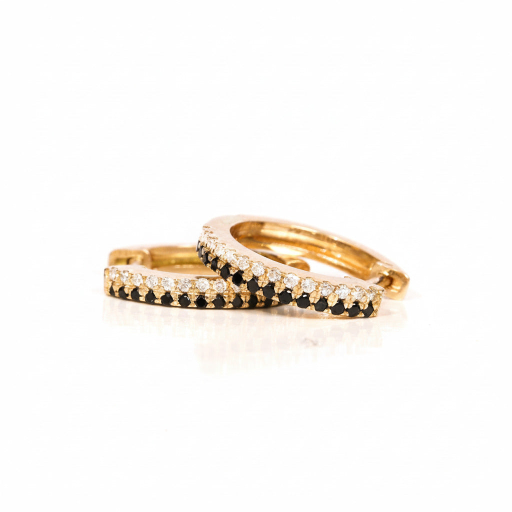 Two gold rings, one with a row of black stones and the other with clear stones, displayed on a white reflective surface with a diagonal 'MINIMAL ATELIER' watermark pattern.
