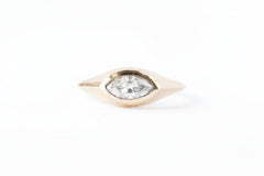 A gold ring featuring a marquise-cut clear gemstone in a marquise-shaped bezel setting, shown on a white background with a repeating 'MINIMAL ATELIER' watermark pattern.