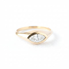 A gold ring with a marquise-cut clear gemstone, photographed on a white textured surface with a repeating 'MINIMAL ATELIER' watermark overlay.