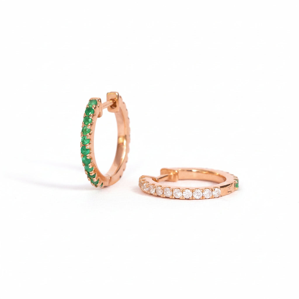 A pair of rose gold hoop earrings, one of which is open to show a row of green gemstones, and the other is closed with a row of clear stones, displayed on a light pink background with a repeating 'MINIMAL ATELIER' watermark.
