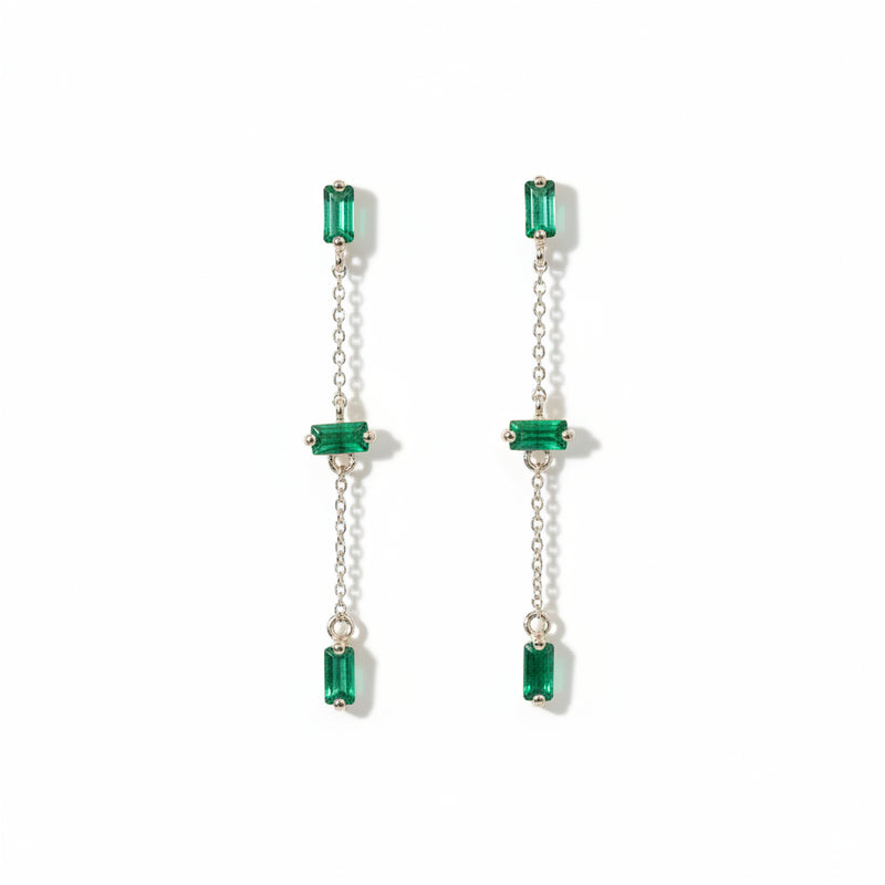 A pair of long drop earrings with rectangular green gemstones and silver-tone chains, displayed on a textured white background with a repeating 'MINIMAL ATTELER' watermark.