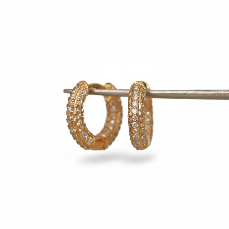 A pair of gold hoop earrings covered in small clear stones, displayed on a metal stand against a light background with a repeating MINIMAL ATELER watermark.