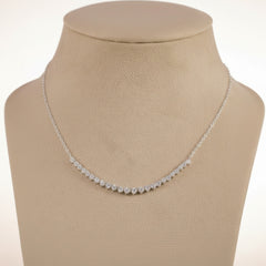 A delicate silver-toned chain necklace with a curved row of small clear stones, displayed on a beige jewelry bust against a light purple background.