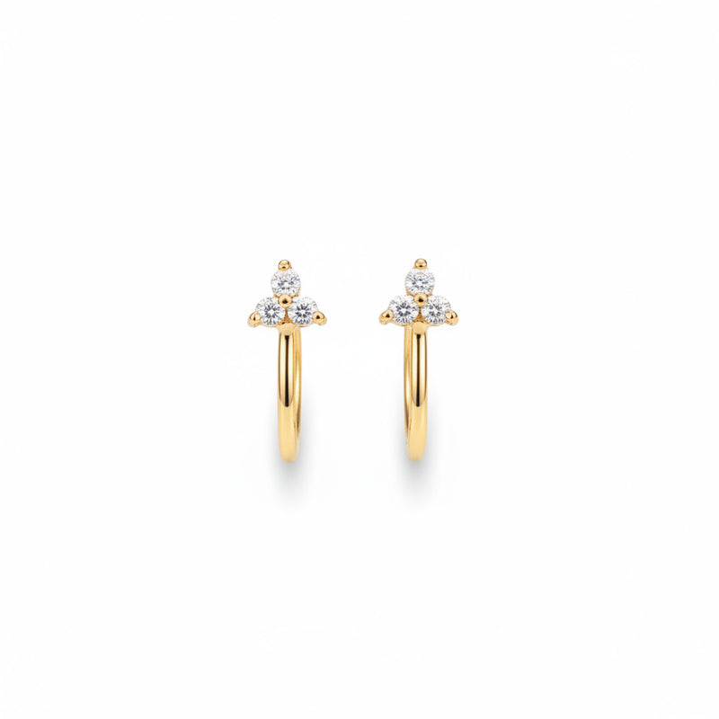 A pair of gold huggie hoop earrings with a small cluster of clear stones at the top, displayed on a beige textured jewelry organizer. The image has a repeating watermark of the brand 'MINIMAL ATELIER'.