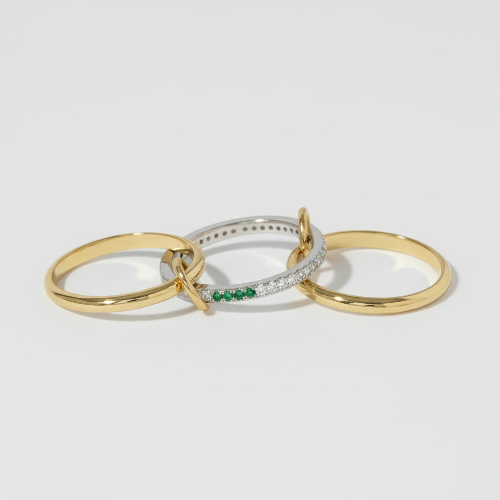 Three minimalist gold-toned rings with a silver ring featuring a green stone accent, displayed on a light background with a repeating watermark.