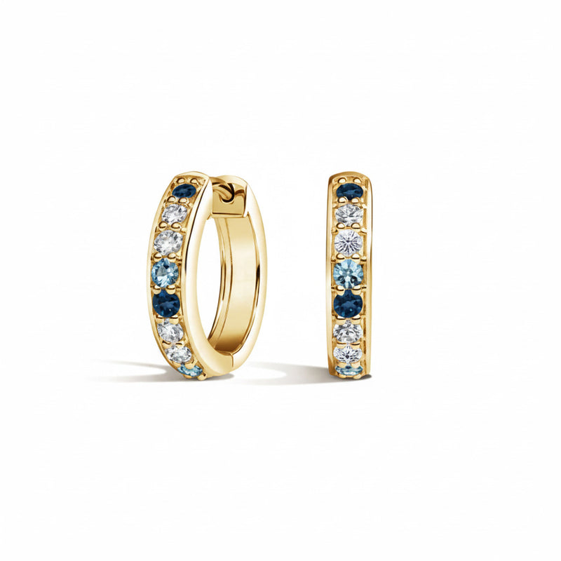 A pair of gold huggie hoop earrings with a channel setting of light blue and clear cubic zirconia stones, shown on a white background with a faint watermark pattern.